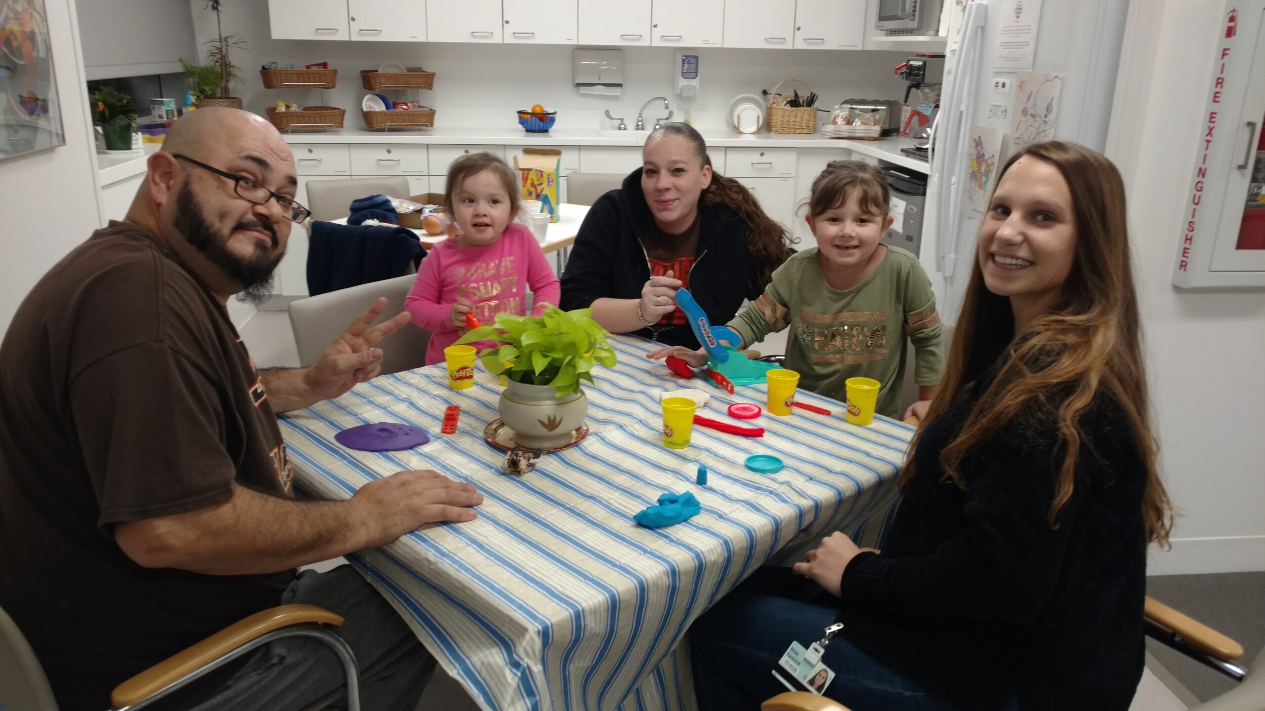 Two families and a staff member play with modelling clay around a table in the Family Room kitchen