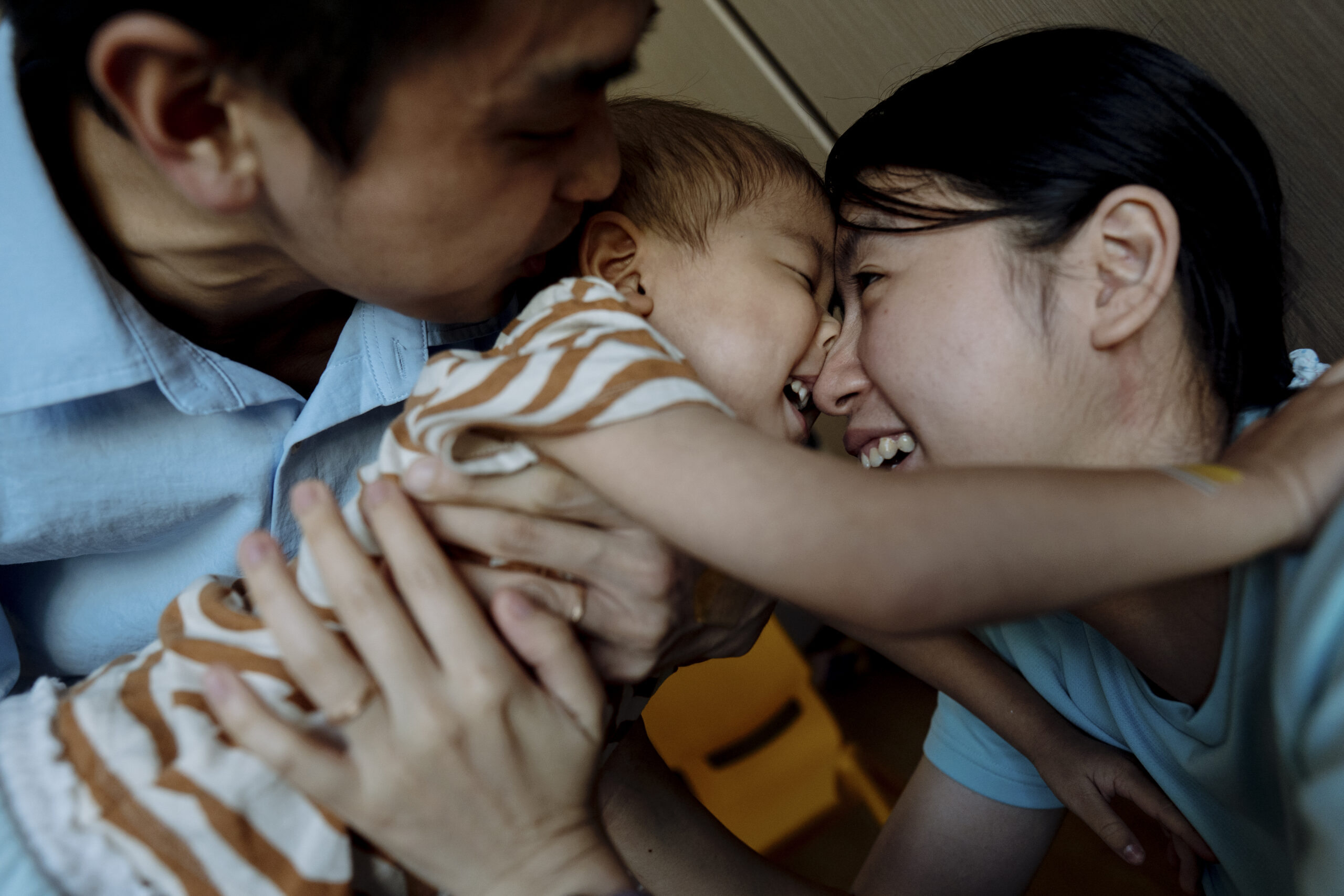 Two parents nuzzle and kiss their laughing baby