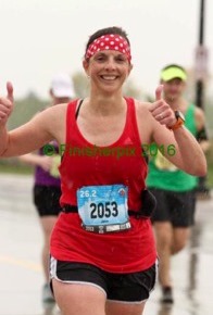 Woman in red shirt runs marathon, gives thumbs up.