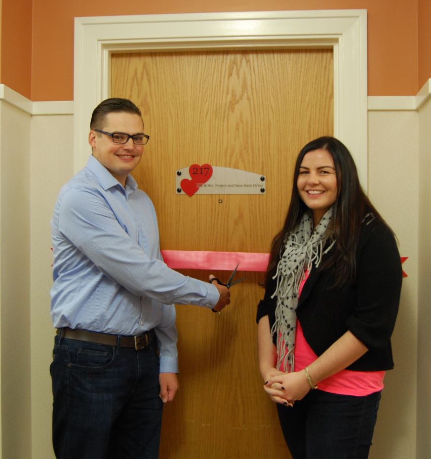 Couple cutting ribbon in front of door