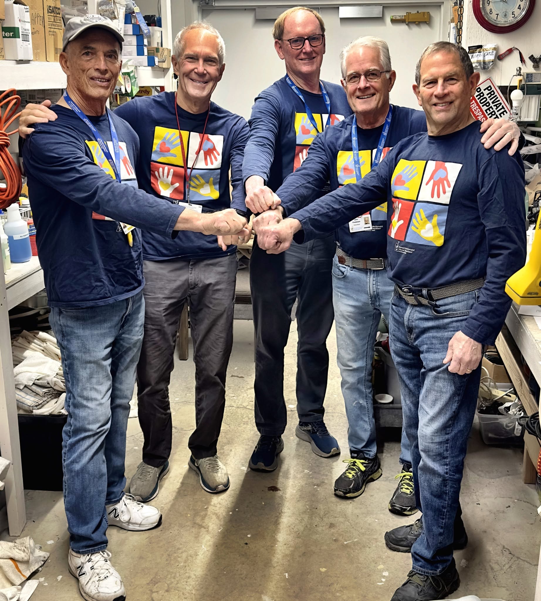 Five volunteers in matching Ronald McDonald House shirts bump fists together in a workshop