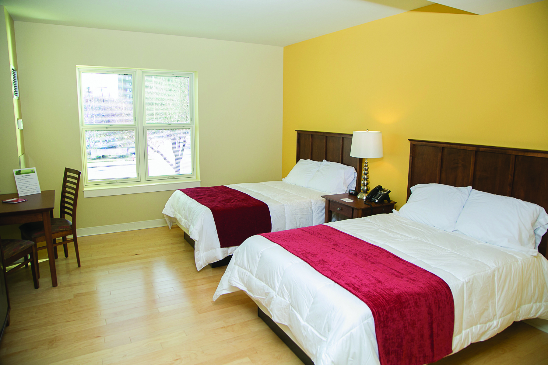 A renovated guest room with two queen beds, a desk, and a window overlooking trees
