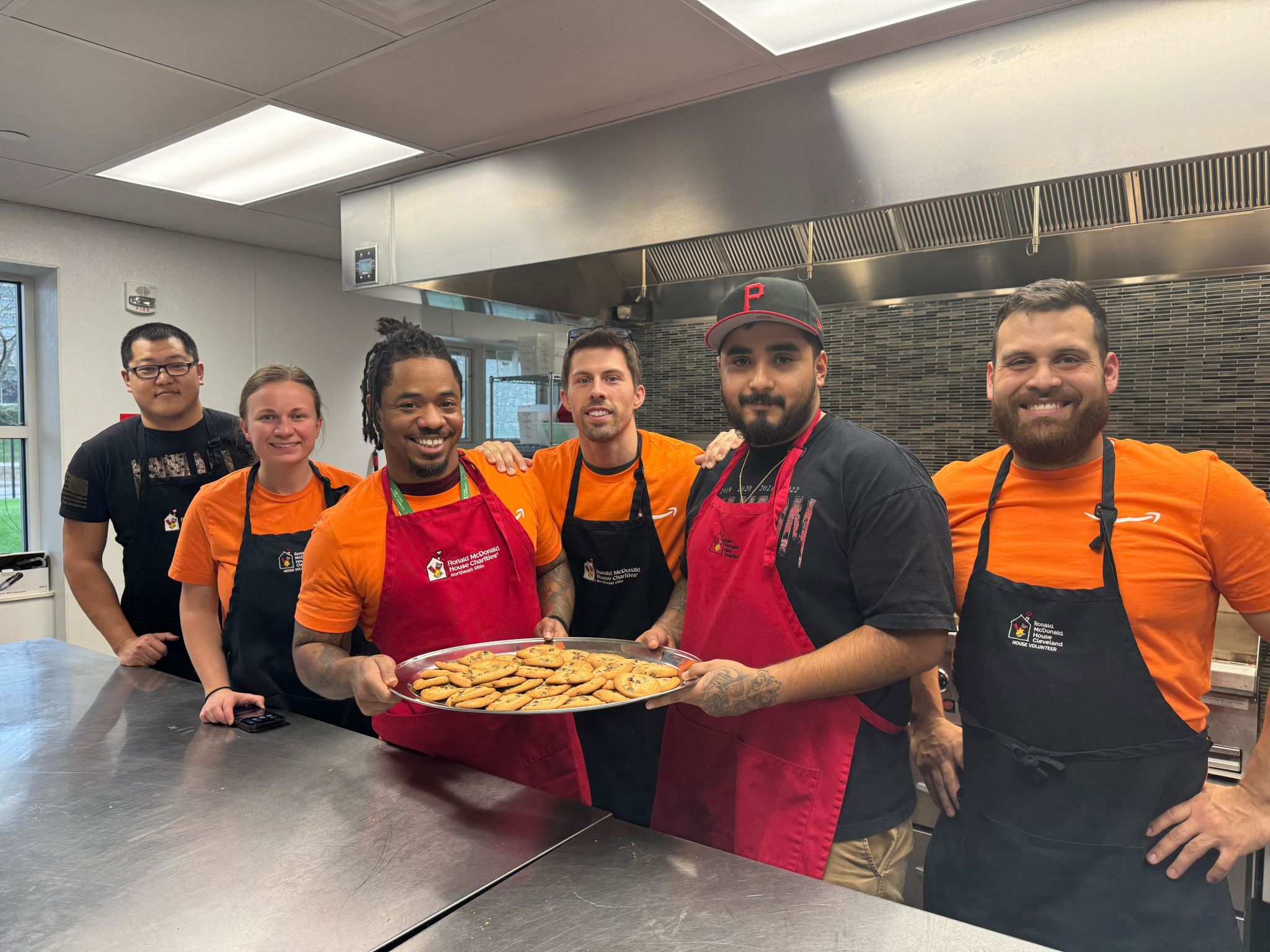 Six volunteers in Ronald McDonald House aprons hold a tray of freshly baked cookies in the House kitchen