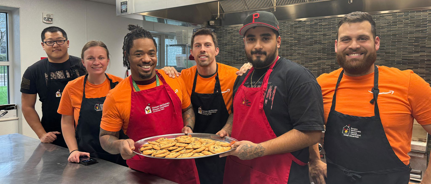 Six volunteers in Ronald McDonald House aprons hold a tray of freshly baked cookies in the House kitchen