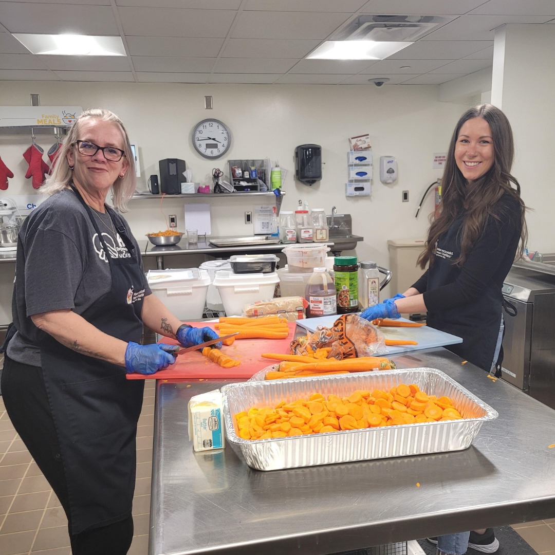 Two volunteers chop carrots in the House kitchen while preparing a meal