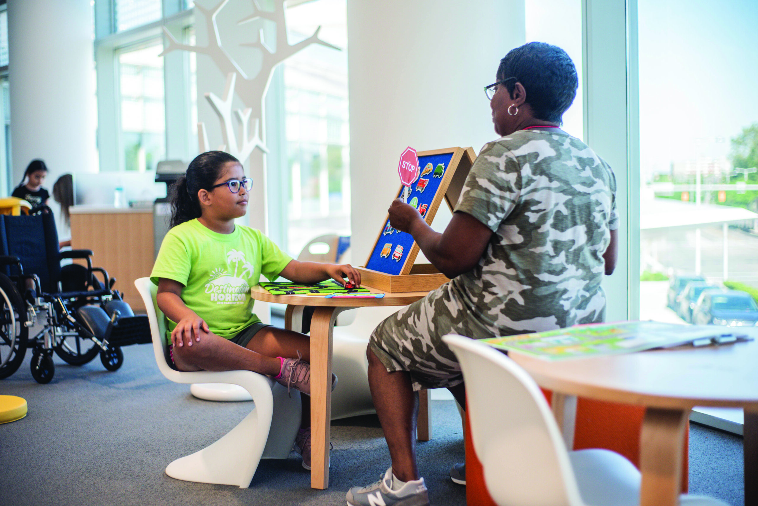 A staff member works with a girl at a table using a picture communication board