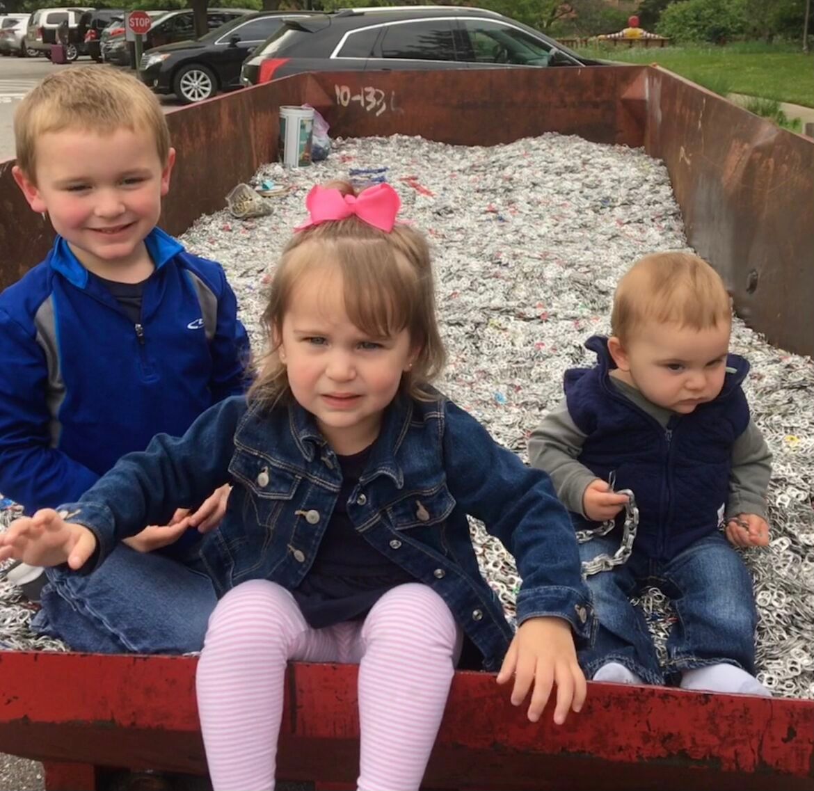 3 children in a recycling bin of pull tabs
