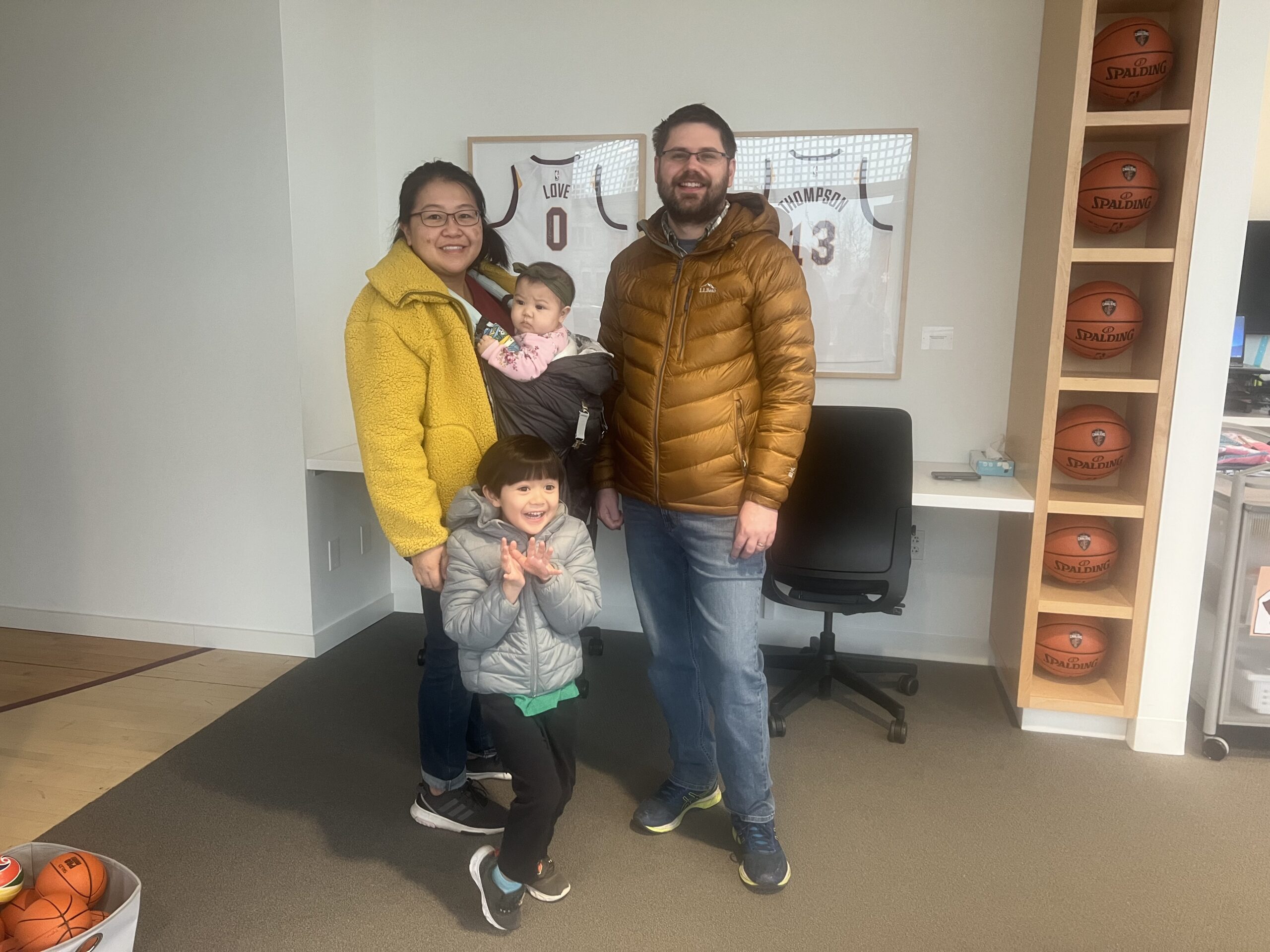 A family of four poses in a room lined with shelves of basketballs