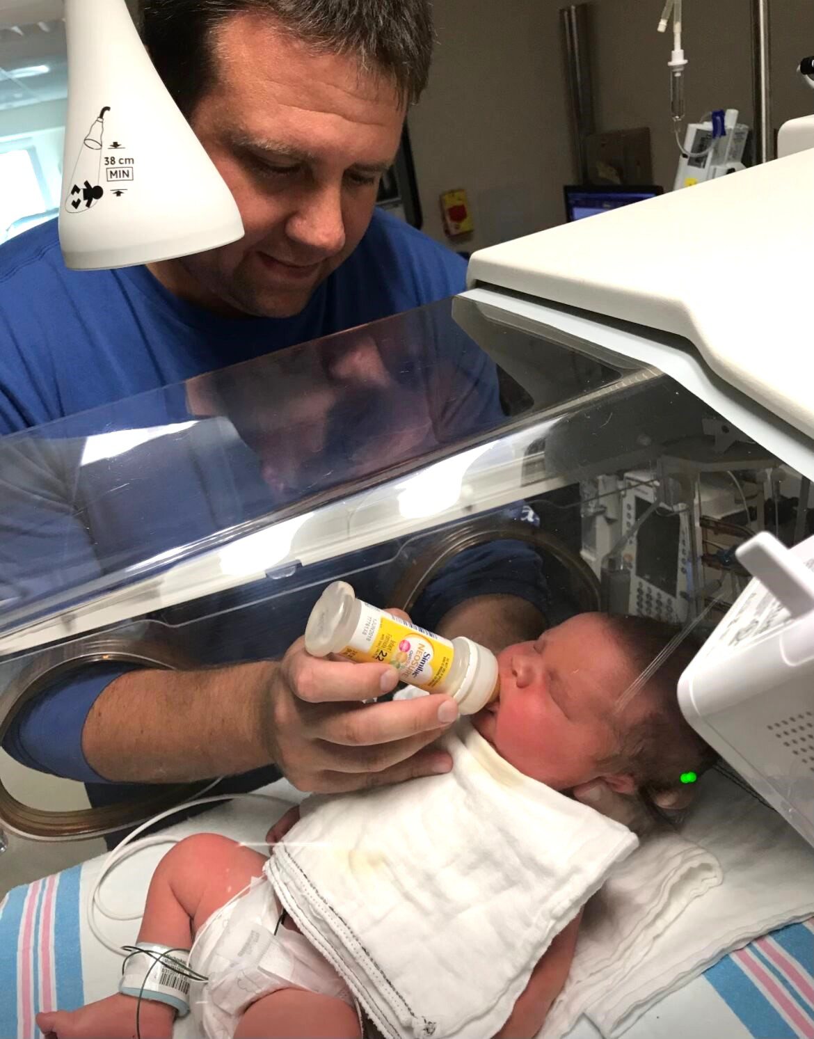 Man feeding baby in isolette with bottle