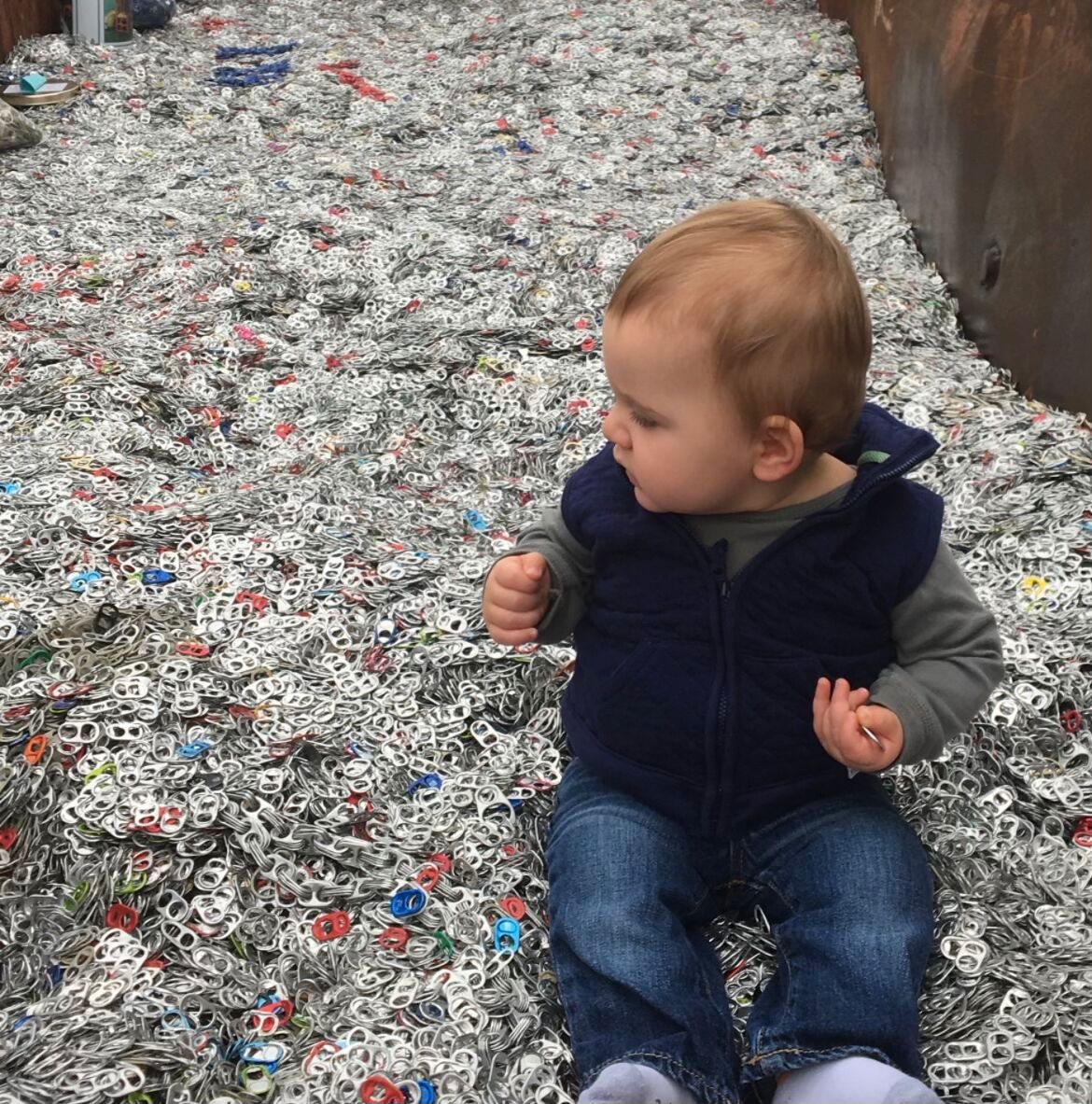 One-year-old boy seated in pull tab recycling bin