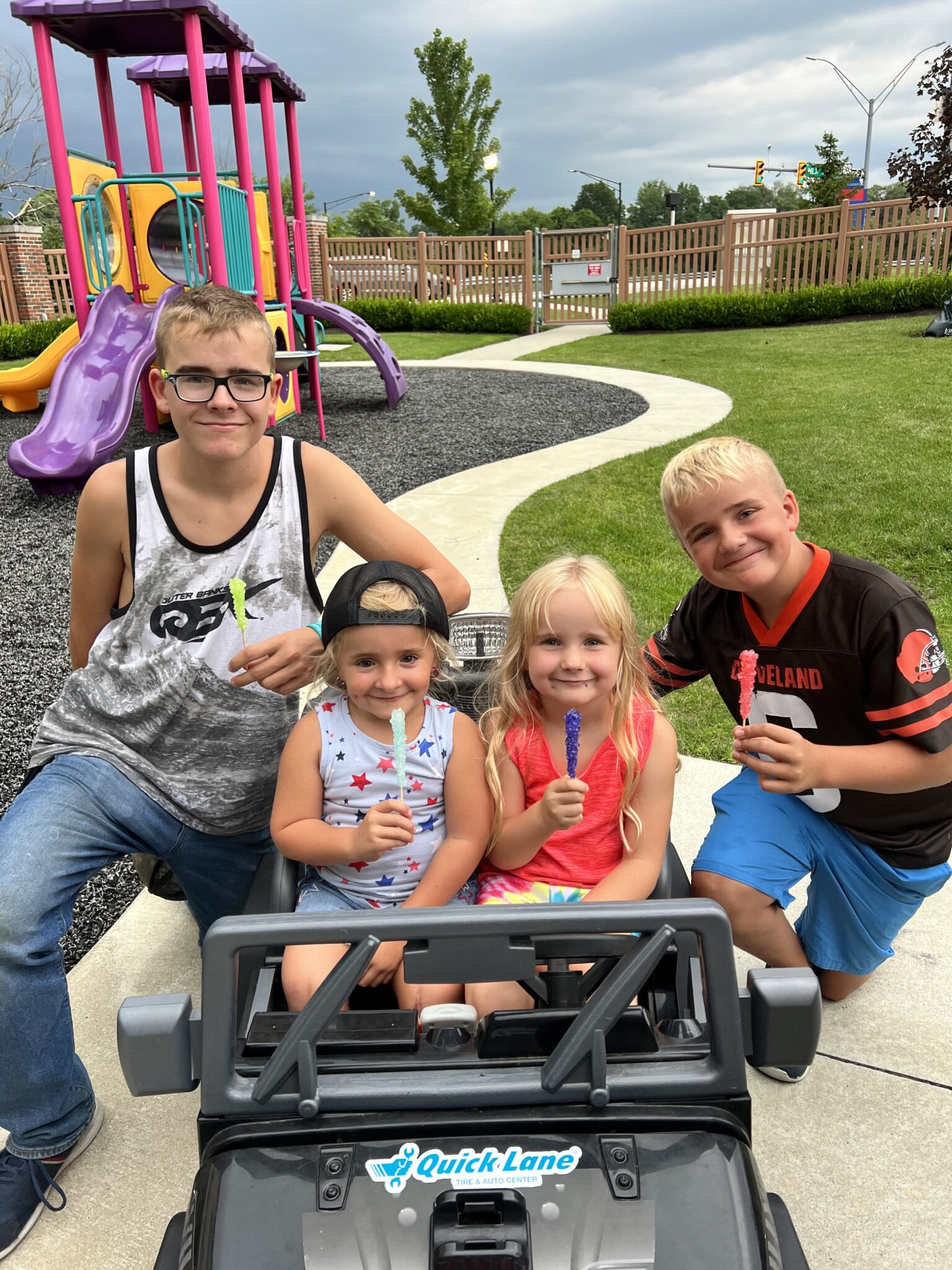 Two girls in power wheels car, boys on either side, on a playground