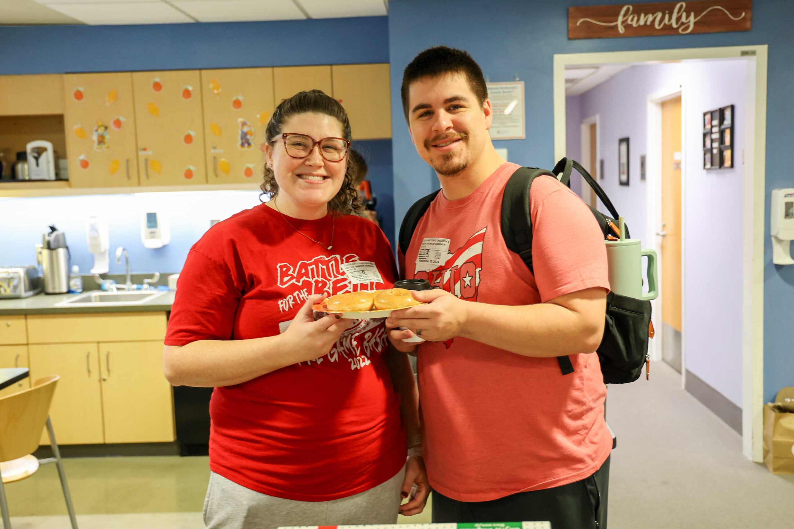 Two people hold plates of doughnuts delivered to a Family Room kitchen