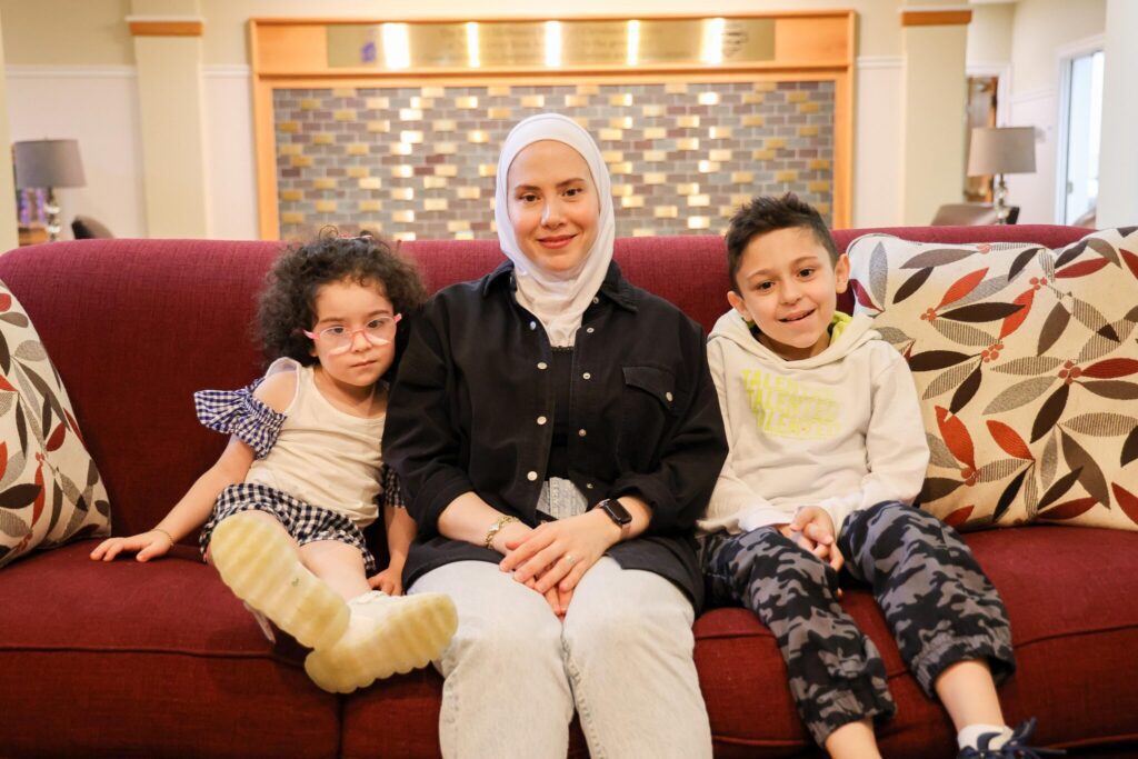 A woman sits on a sofa with two children in a House living room