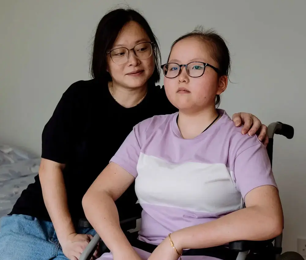 A woman sits with her arm around a teenage girl who uses a wheelchair