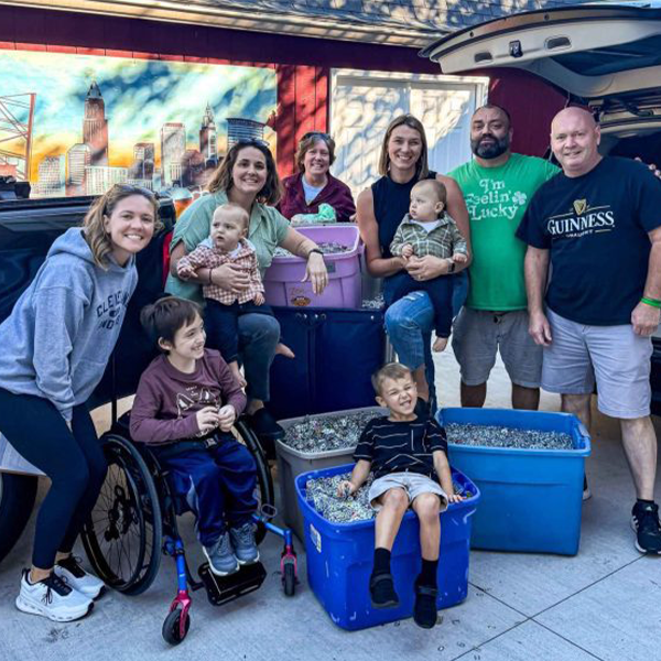 Families and volunteers gather around bins of collected pull tabs at a drop-off
