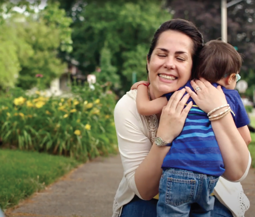 A woman hugs a young child tightly, smiling, on a garden path