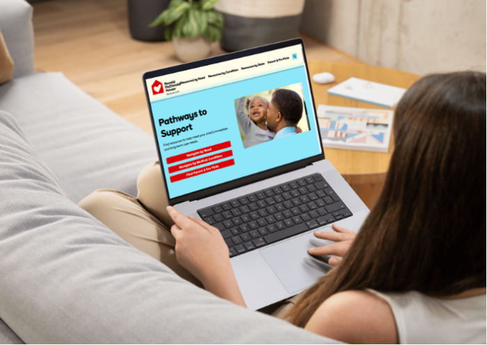 A person on a couch browses the Ronald McDonald House Resource Link 'Pathways to Support' site on a laptop