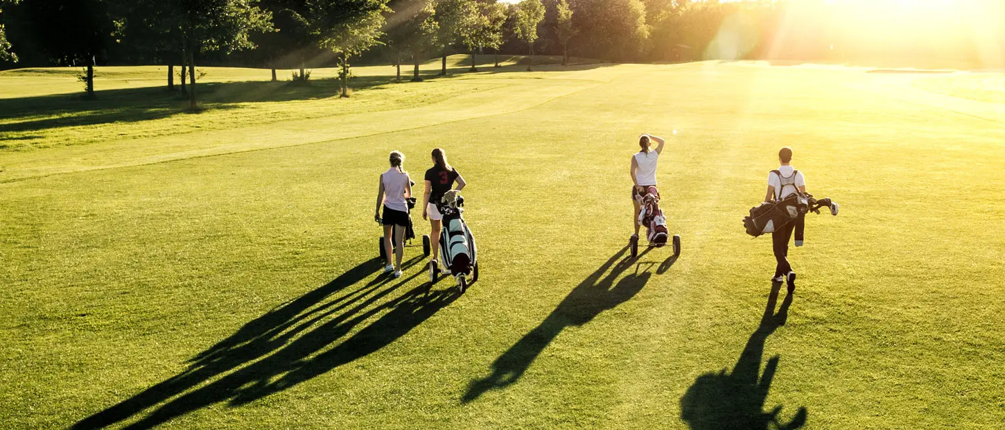 Four golfers walking a fairway at sunset, pulling their clubs behind them