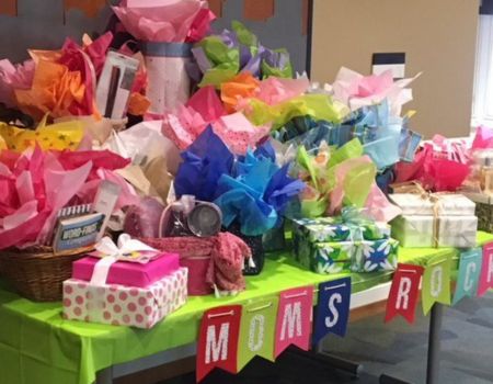 A table with many boxes of presents wrapped with bows and a sign on the front of the table says "moms rock"