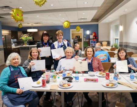 The Guardians of the Community Volunteer Group are seated at a lunch table with food and they're holding up their award certificates