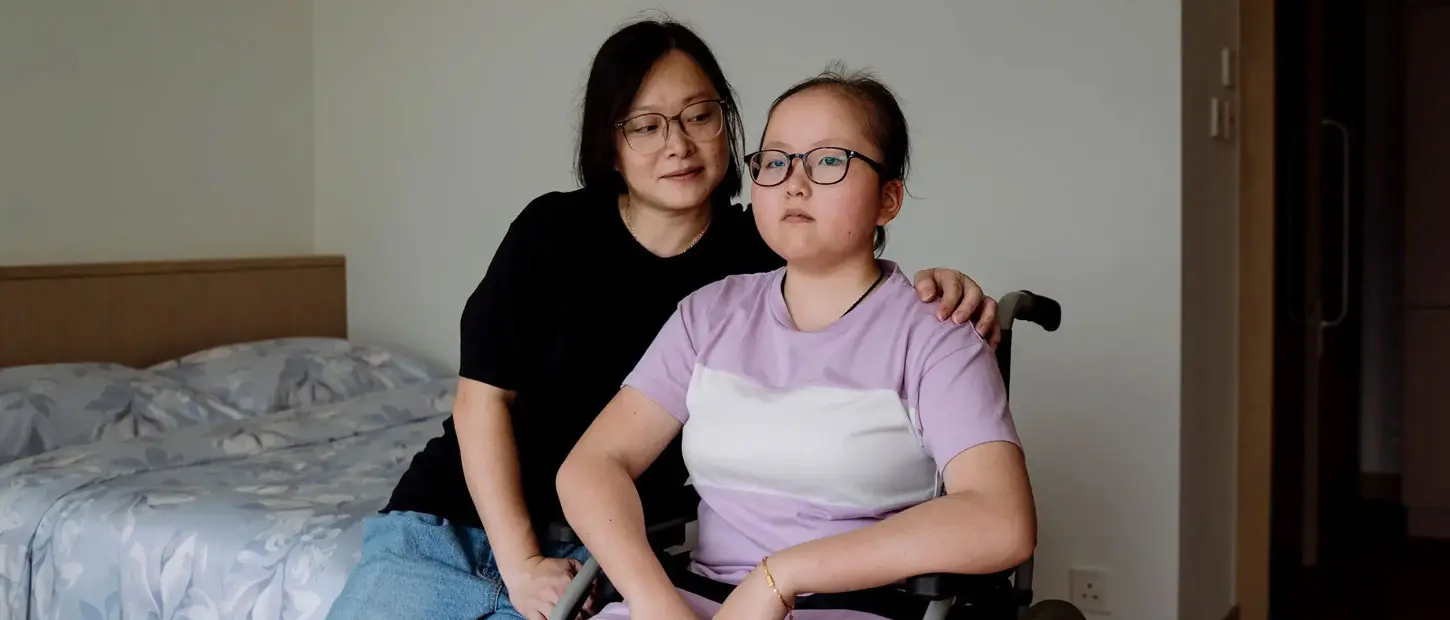 A woman sits with her arm around a teenage girl who uses a wheelchair
