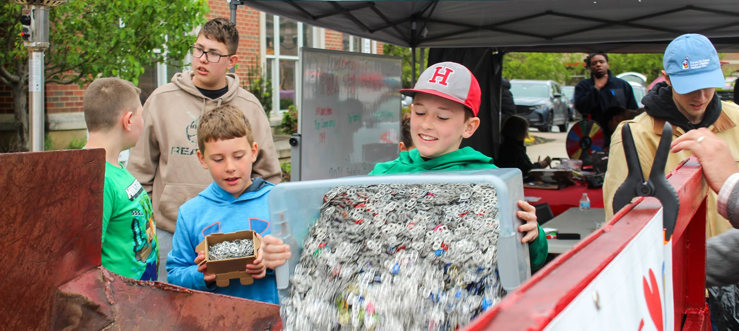 Children empty a bin of collected pull tabs into a collection container at a drop-off event