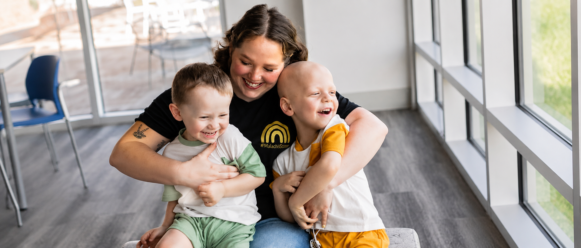 A woman laughs as she hugs two young boys in a family room