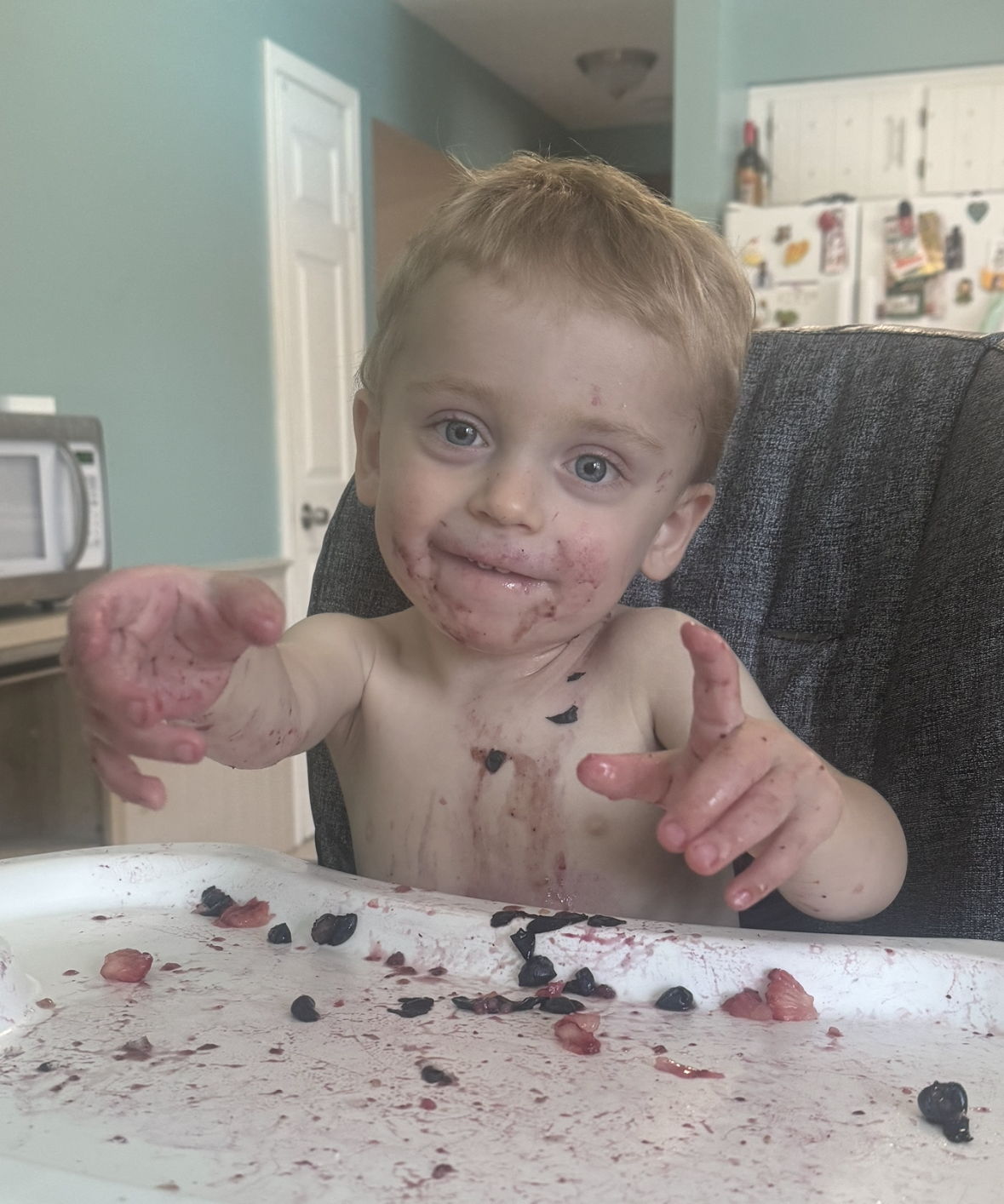 little boy in high chair with messy blueberries