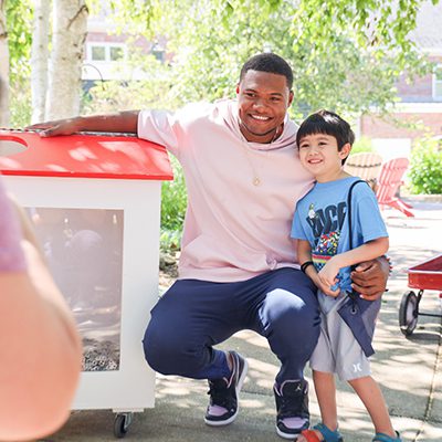 Cleveland Guardians player Oscar Gonzalez kneeling next to a pull tab collection house with a young boy.
