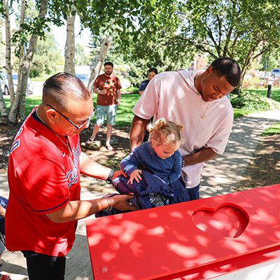 Cleveland Guardians player Oscar Gonzalez and a dad help a young boy put pull tabs in the collection bin